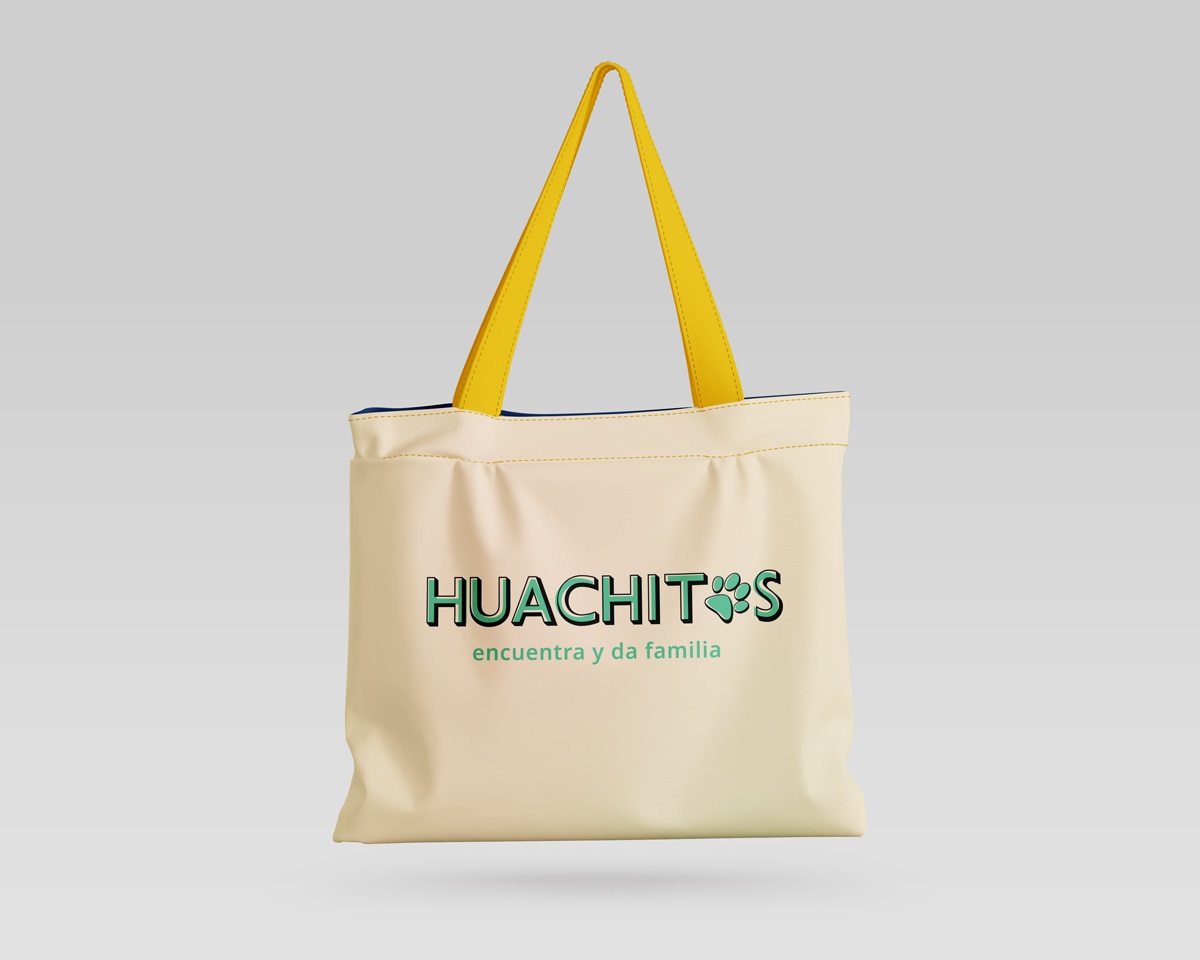 Fotografía de un bolso de tela tipo totebag de color amarillo claro, con el logo de Huachitos y su tagline: Encuentra y da familia en sus colores verdes originales.